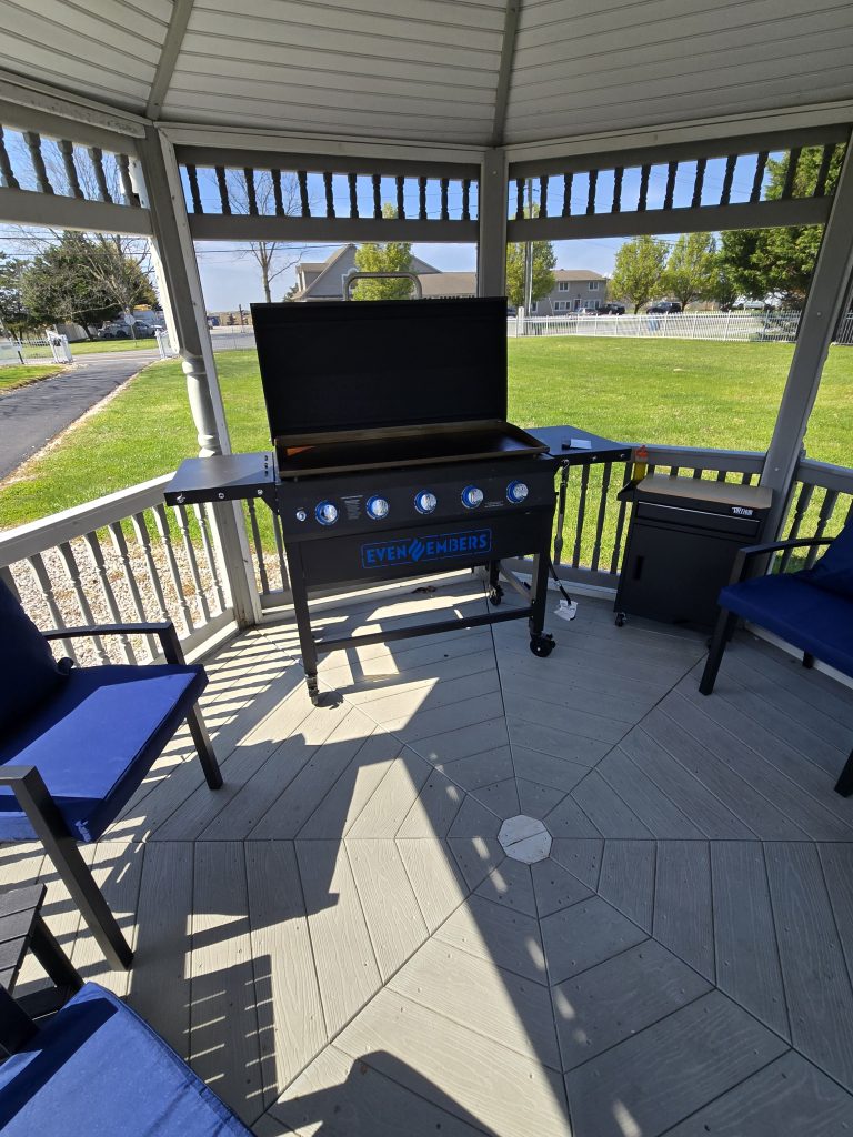 Outdoor grill setup under a gazebo with seating and green lawn