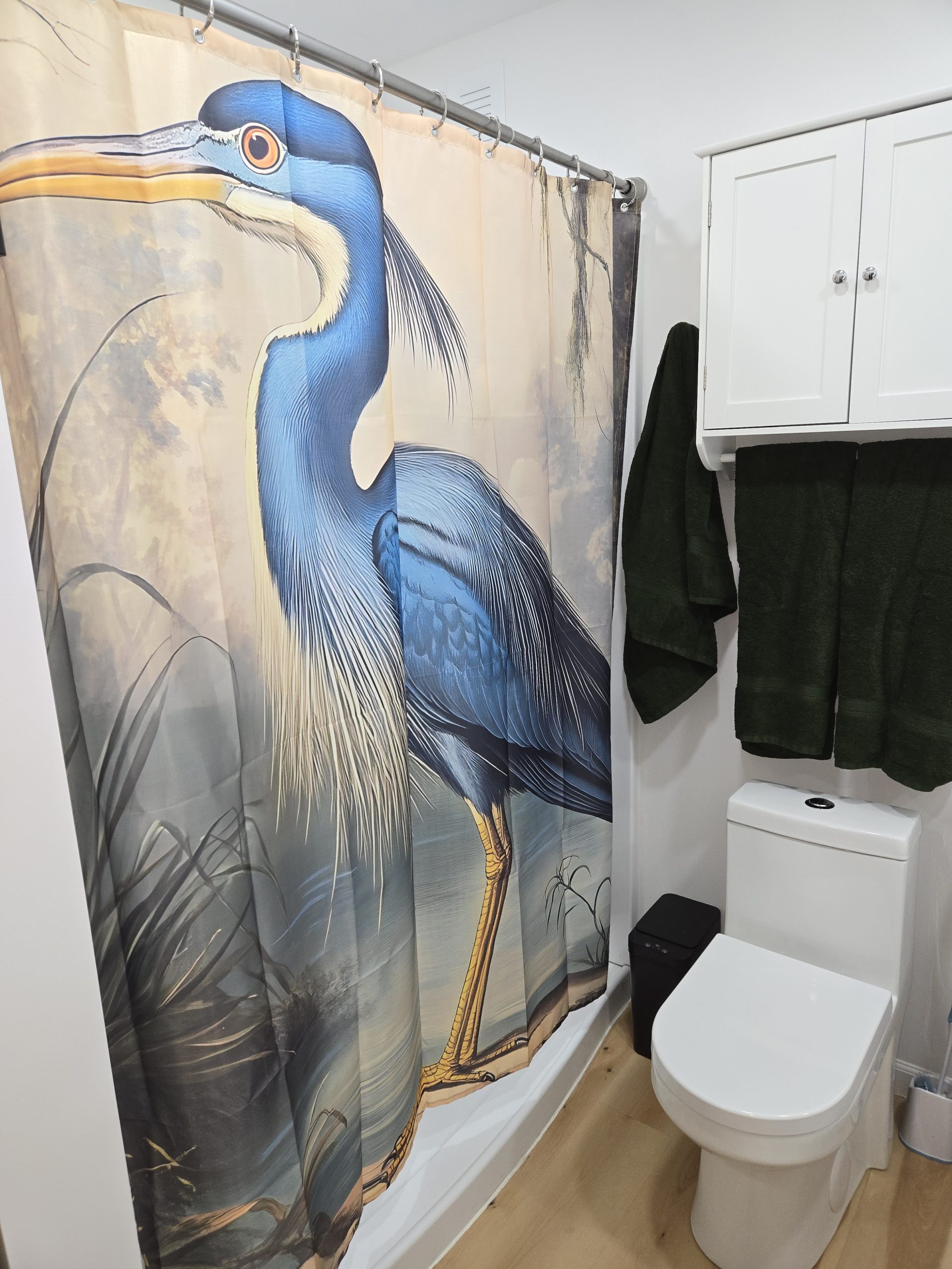 Heron bathroom interior featuring a unique heron shower curtain, toilet, and storage cabinet.