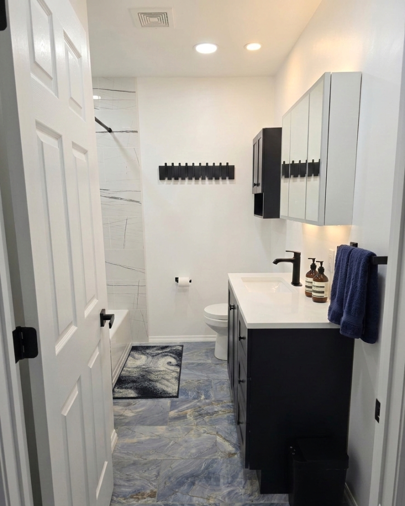 Stylish main bathroom with blue tile floor, white vanity, and modern black fixtures. Photo gallery.